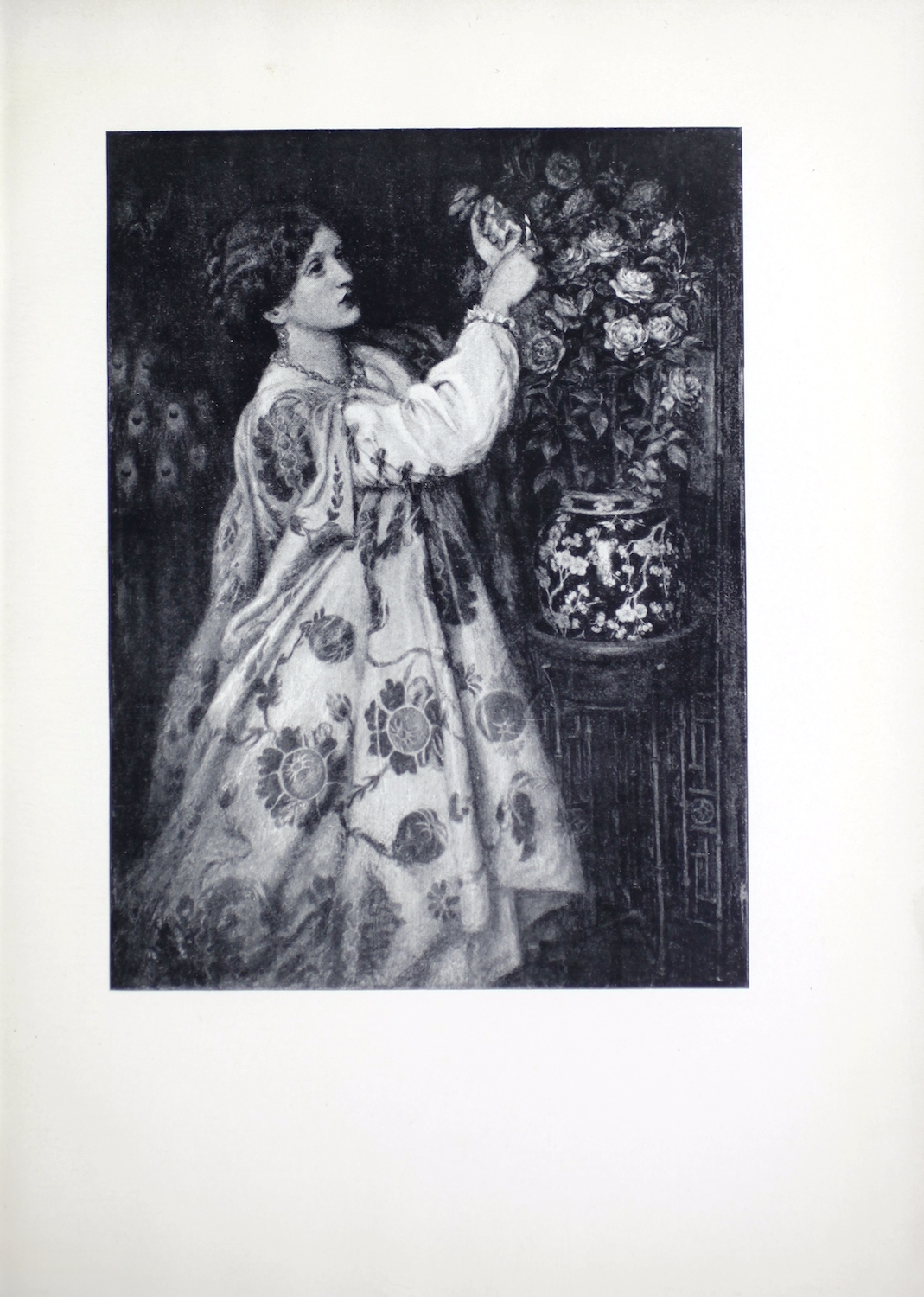 This black and white reproduction of Rossetti’s painting is of a woman, portrayed by Mrs. F. R. Leyland, arranging roses at home. The woman is in three-quarter profile and wears an elaborate floral dress with puffed sleeves. Her hair is tied in a braid behind her head. She arranges a large bouquet of flowers in a Japanese-inspired ceramic vase (blue and white export porcelain). The vase rests in a terra cotta pot on a bamboo plant stand. It sits in the corner of a room. The dark walls (green in the original oil painting) fill the background with two bags hanging behind the woman’s head to the left of the image. The larger bag features a peacock pattern that is still visible in this reproduction. The smaller blue bag above it blends into the background.