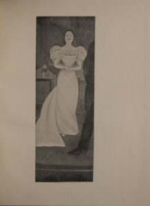 The image is of a woman standing on a stage She wears a long white dress with a train and is standing with hands clasped Her hair is pulled back and her face shows emotion she may be singing or weeping The back leg and left arm of a man stands in front just to the right of her He wears a dark suit At the bottom of the frame there is the suggestion of men s hats below edge of stage There are indistinguishable objects in the background on stage The image is vertically displayed